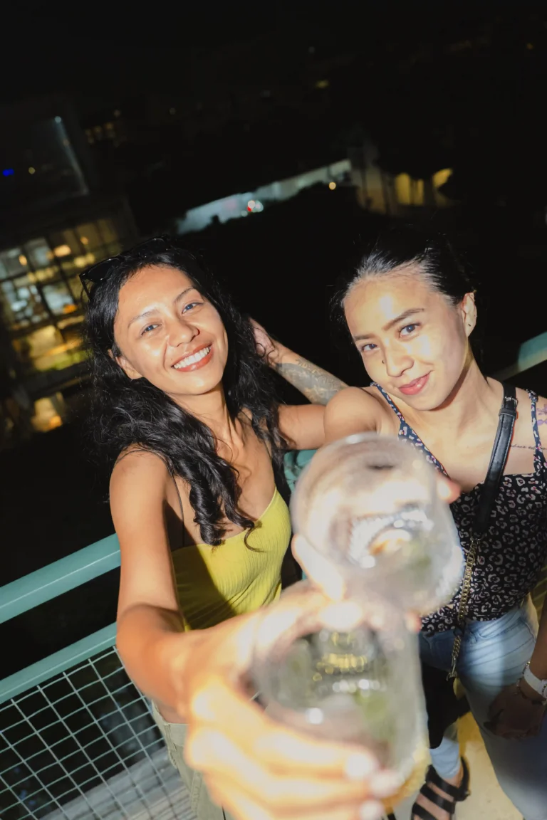Two women friends toasting with drinks at a night event at at06 in Canggu.