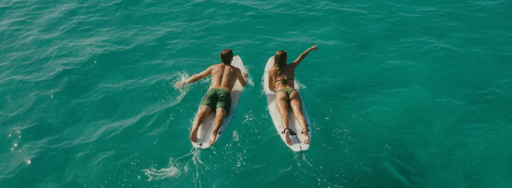 Aerial view of a couple paddling on surfboards in the clear turquoise waters near Echo Beach, Canggu, Bali, enjoying the active lifestyle.