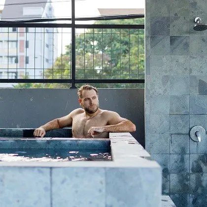 A man relaxing in an outdoor hot tub or plunge pool at at06 in Canggu, Bali, with a city view in the background.