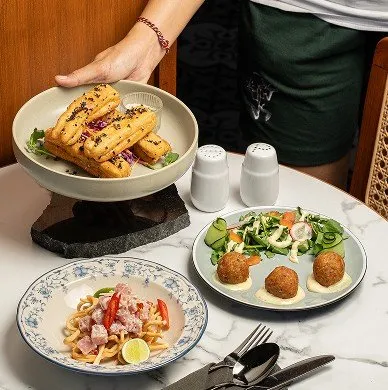 A table laden with various dishes, including fried sticks, pasta, and arancini-like balls, at AT 06 restaurant in Canggu, Bali.