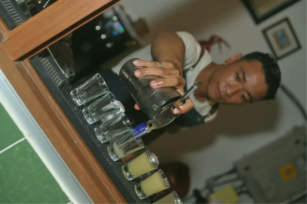 A skilled bartender at the locally-owned at06 fusion restaurant in Canggu pouring vibrant yellow shots, embodying the work and workout Bali lifestyle.