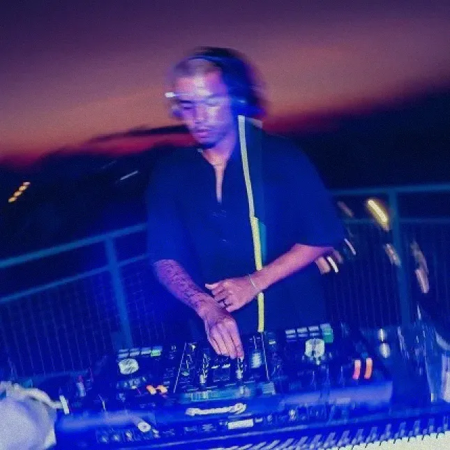 A DJ with bleached hair performing a set at an outdoor event in Canggu at sunset.