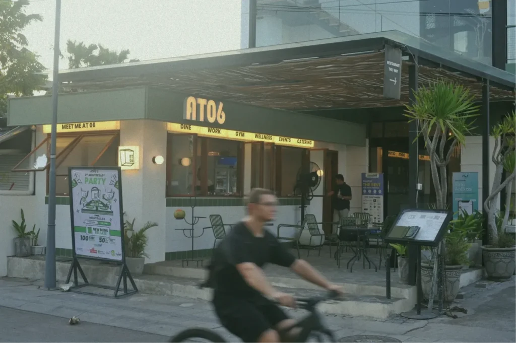 The exterior of the at06 building in Canggu, with a sign listing its services: Dine, Work, Gym, Wellness, Events, and Catering.