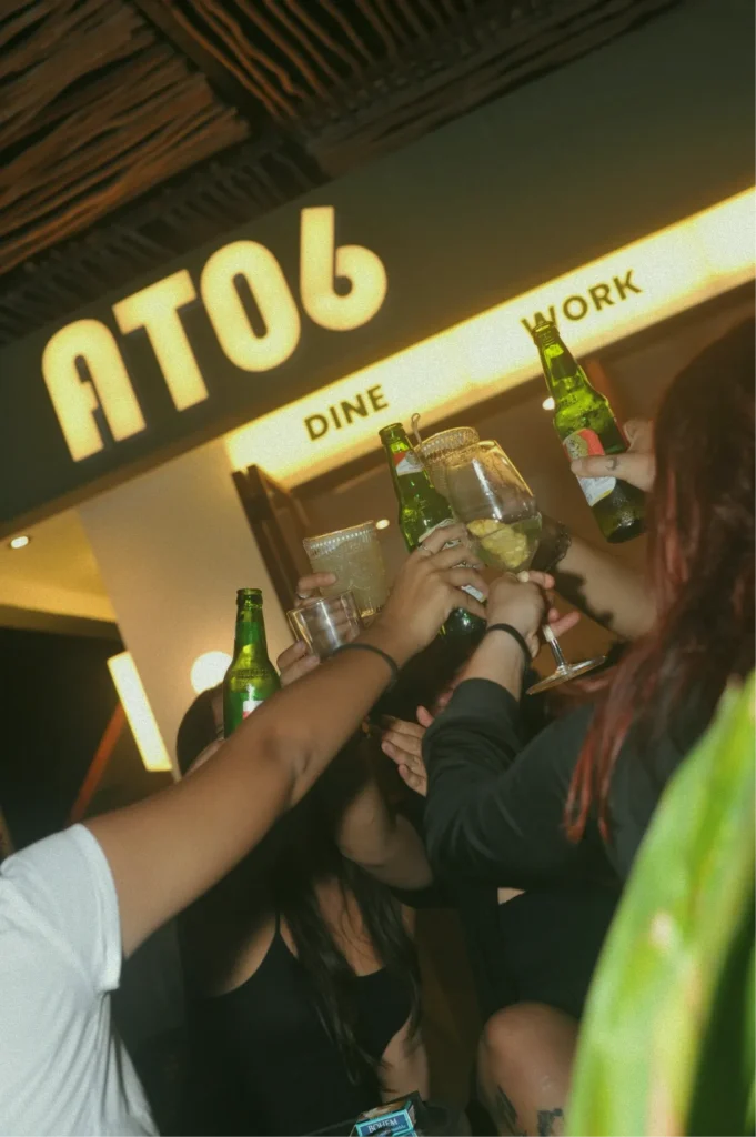 A group of people toasting with beers and cocktails at the at06 bar in Canggu.