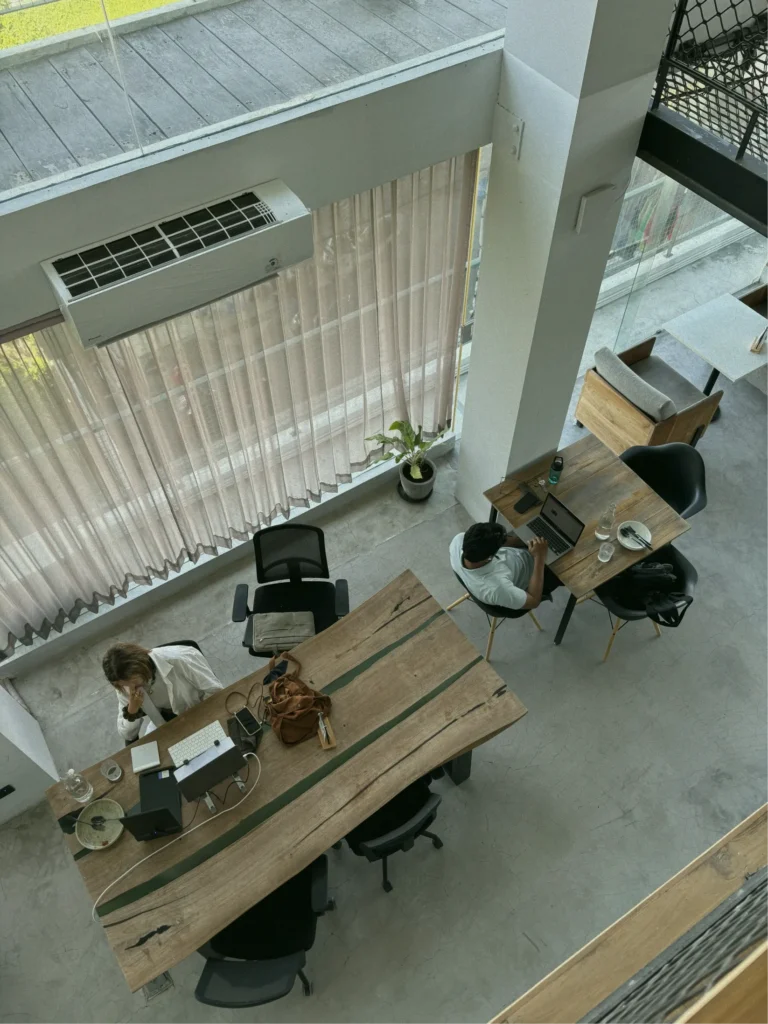 A high-angle view of two people working on their laptops in a modern co-working space in Canggu.