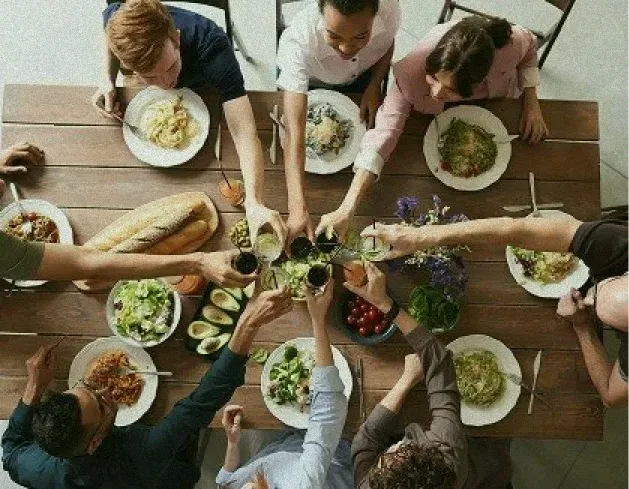 An overhead view of a group of people toasting with drinks over a large dinner table in a Canggu restaurant.