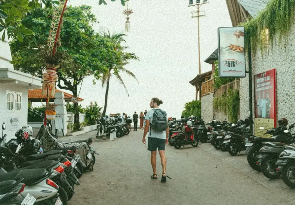 Best Restaurants Canggu: The Lunch Guide for Active Travelers 1 A man with a backpack walks down a crowded street in Canggu, Bali, lined with parked motorbikes on both sides