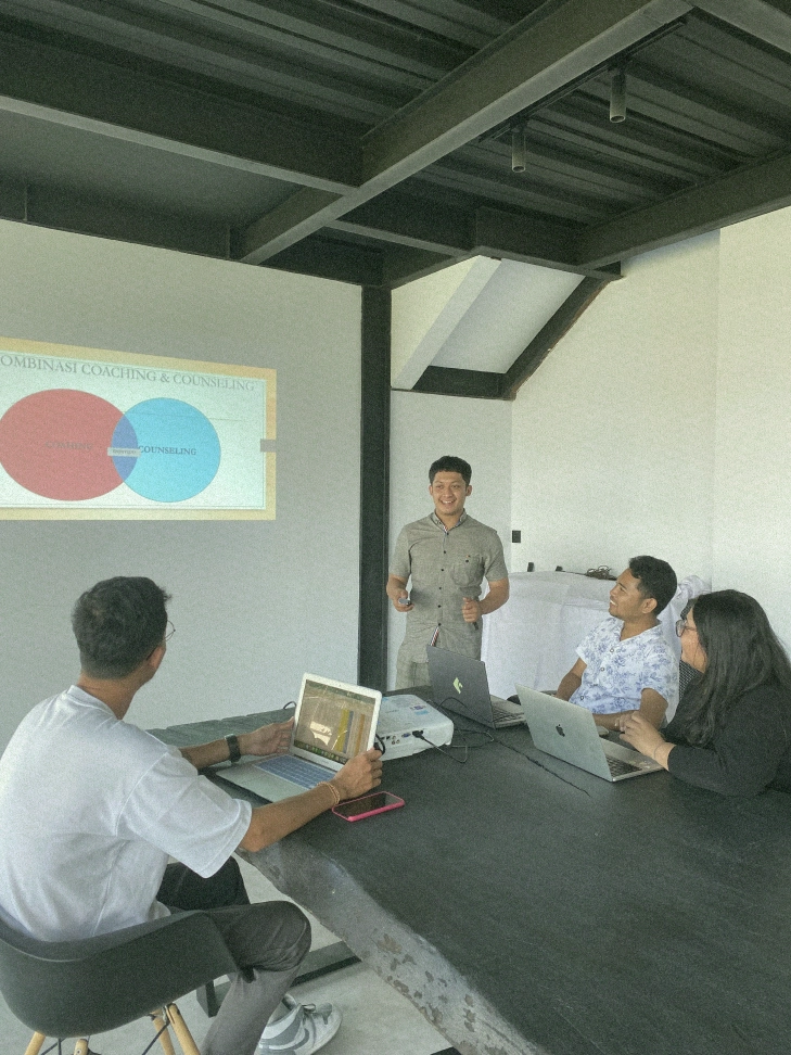 A presenter leading a meeting or coaching session in a Canggu coworking space, with a "Coaching & Counseling" Venn diagram projected.
