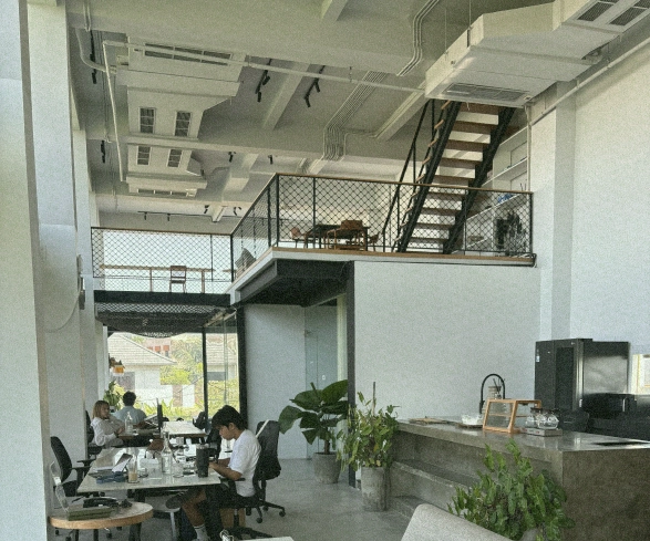 Digital nomads working in a modern coworking space in Canggu, with a view of the bar area and mezzanine level.