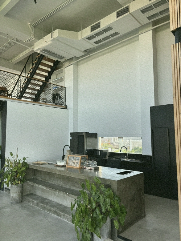The modern kitchen and bar area of a Canggu coworking space, featuring a large concrete island and views of the mezzanine.