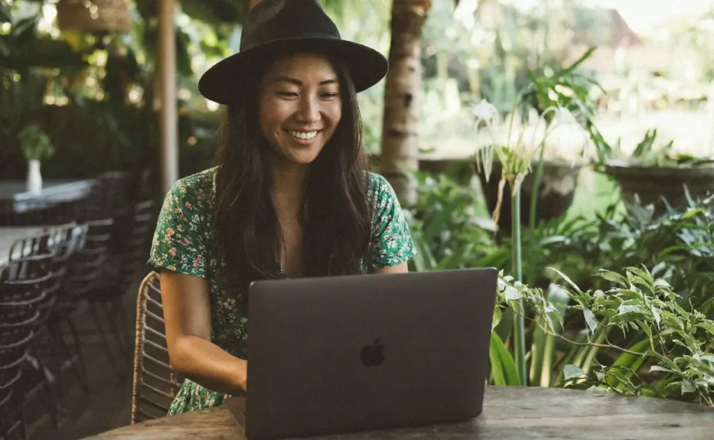 The Financial Mechanics of Living in Canggu: A Digital Nomad Guide 1 Smiling digital nomad wearing a hat working on a laptop at an outdoor cafe in Canggu